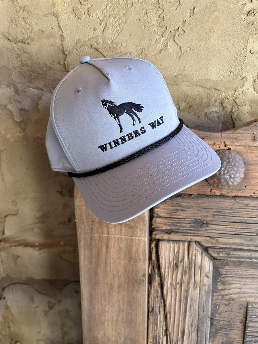 Grey cap with Winners Way horse logo resting on the corner of a wooden frame.