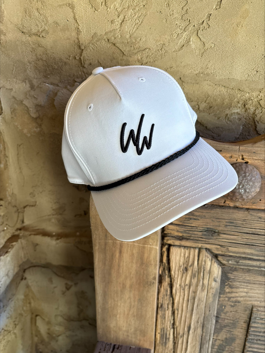 White cap with the Winners Way "WW" icon in black resting on the corner of a  wooden frame. 